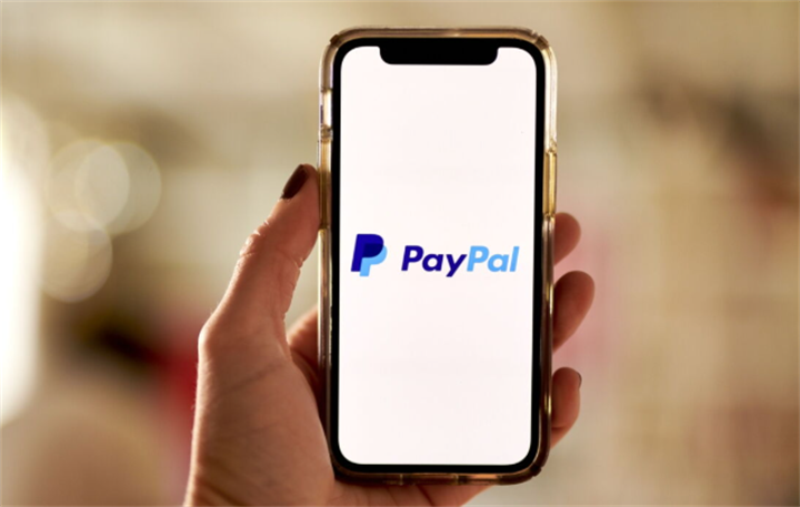 Hand holding a smartphone displaying the PayPal digital payment platform logo