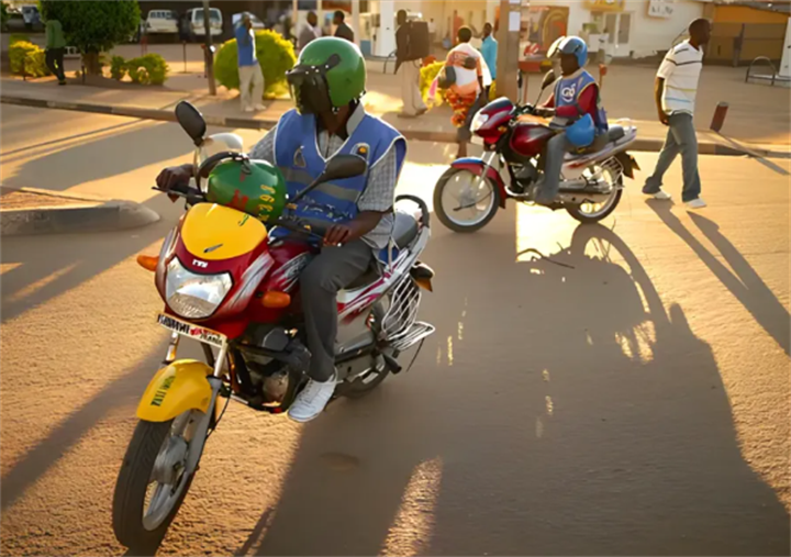 Motorcycle taxi riders in vests operating two-wheeler transport on an African town road, comparable to Southeast Asia’s bike delivery fleets