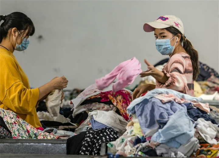 Two female workers sorting piles of pre-loved garments in a secondhand textile processing factory