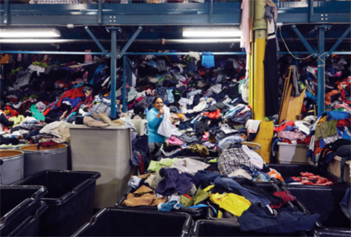 Warehouse sorting facility filled with massive piles of unsorted donated secondhand clothing, a key node in used apparel global supply chains