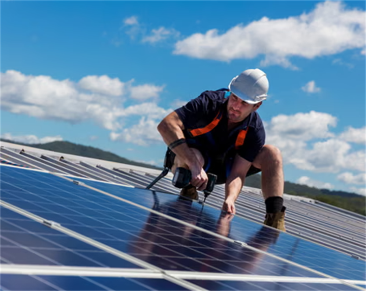 Technician installing rooftop solar panels under clear blue sky, showing a household renewable solution to offset high electricity prices