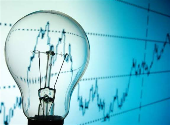 Clear lightbulb overlayed over rising financial stock charts, illustrating climbing global electricity cost trends for residential users