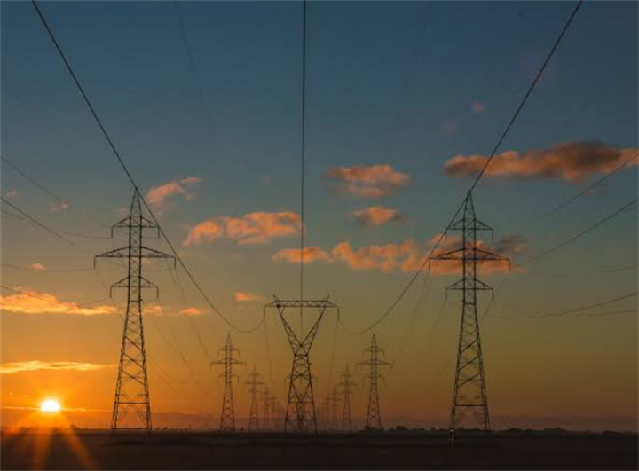 High voltage power transmission pylons silhouetted at sunset, representing national cross-country electricity grid infrastructure that shapes regional power pricing
