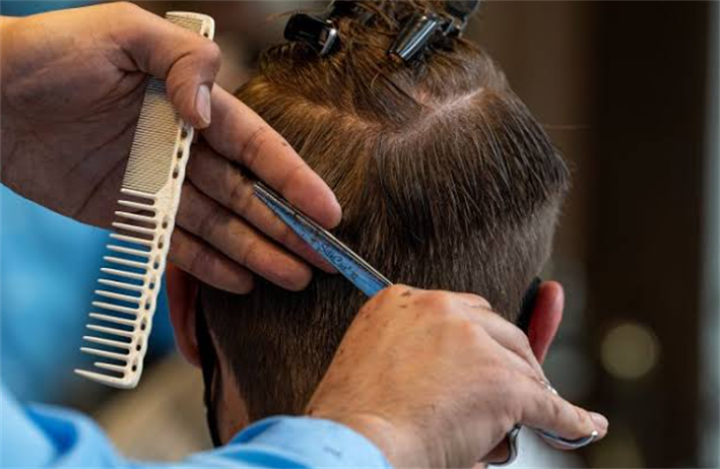 Barber trimming men's short hair with comb and scissors inside a salon