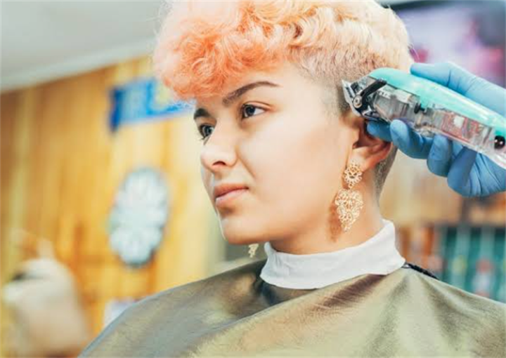 Hairstylist using electric clippers to create an undercut for a young woman in a barbershop