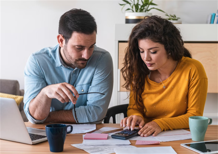 Couple calculating household debts and reviewing financial paperwork at home desk