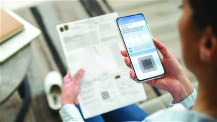 Person holding a paper invoice and smartphone showing a fake QR payment screenshot used in financial scam