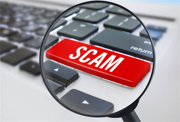 Magnifying glass focusing on a red keyboard key printed with 'SCAM', symbolizing online financial fraud detection