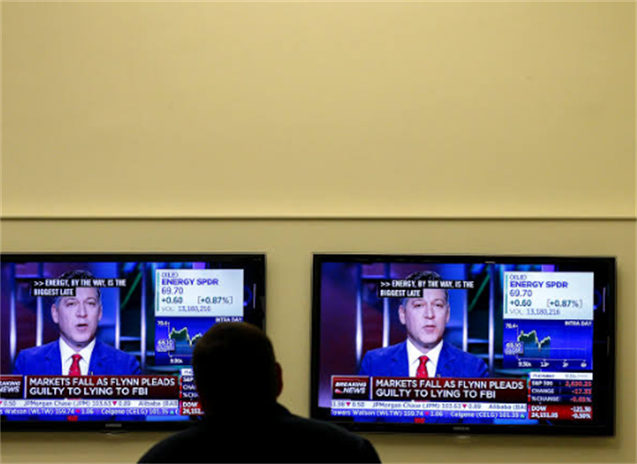 Person watching identical cable news broadcasts on two wall-mounted TVs, illustrating replicated manipulated financial media content