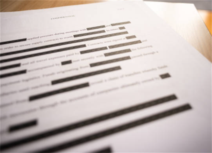 Redacted printed official paperwork with blacked-out text blocks, showing the format of genuine government documents