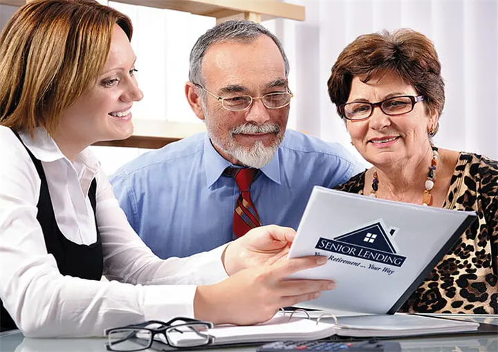 Female lending agent reviewing senior housing loan paperwork with an elderly couple, illustrating legitimate vs fraudulent reverse mortgage consultations