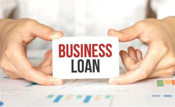 Two hands holding a card printed with Business Loan text over financial growth charts